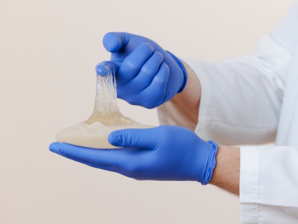 A breast implant being held by a surgeon whilst it has been cut open